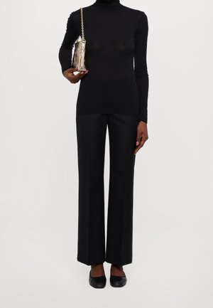 Černý rolák a široké černé kalhoty, doplněné kovovou taškou s řetízkovým popruhem a plochými černými botami.