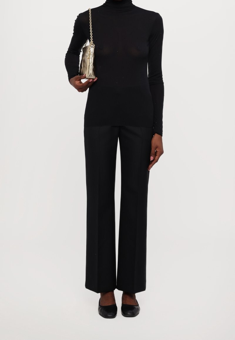 Czarny golf i szerokie czarne spodnie, zestawione z metaliczną torbą z łańcuszkowym paskiem oraz płaskimi czarnymi butami.