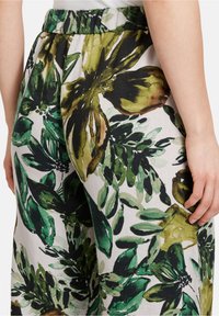 Květinové kalhoty se širokými nohavicemi, vyrobené z lehkého materiálu s zeleno-černým vzorem listů na světlém pozadí.