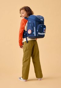 Sac à dos bleu marine avec un design sur le thème de l'espace, deux poches latérales et des bretelles rembourrées, porté par un enfant en chemise à manches longues orange et crème.