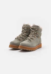 Bottines en daim vert clair avec un col rembourré, œillets en métal et semelle extérieure en caoutchouc épais. Présente des lacets beiges et une bordure en fourrure douce.