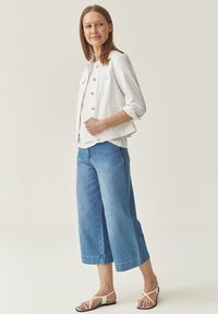 White denim jacket with button closures, paired with wide-leg light blue denim cropped pants and white sandals with a strap design.