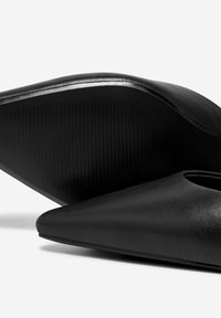 Scarpe slip-on in pelle nera con punta affusolata e silhouette curva. Suola testurizzata con scanalature per una presa migliore. Finitura liscia complessiva.