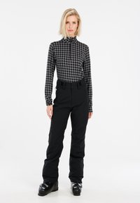 Schwarze Skihose mit hoher Taille, kombiniert mit einem eng anliegenden Langarmshirt im Hahnentrittmuster. Glatte Textur und funktionale Reißverschlusstaschen.