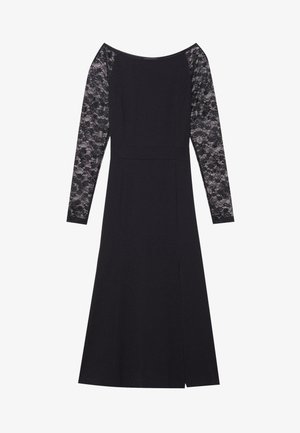 Svart kjole med tettsittende liv, lange ermer i blonder, og en liten sprekk foran. Stoffet er glatt og elastisk, i kontrast til blonden.