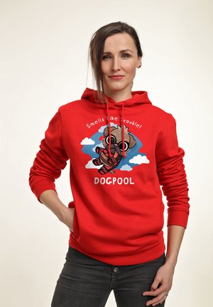 Kobieta ubrana w czerwoną bluzę z kapturem z kreskówkowym psem przebranym za Deadpoola z tekstem "Smells like trouble! DOGPOOL" na białym tle.