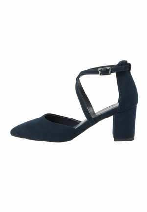 Zapato de tacón bajo de bloque para mujer en ante azul marino con correas cruzadas en el tobillo y una hebilla plateada sobre fondo blanco.