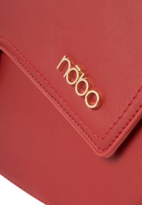 Borsa a tracolla in ecopelle rossa con chiusura a pattella, hardware dorato con logo impresso e cuciture a contrasto lungo i bordi.