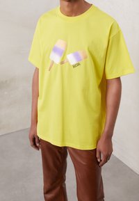 Camiseta de algodón amarilla con un gráfico de dos helados en colores pastel. Corte holgado con mangas cortas y escote redondo.