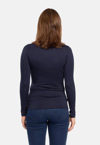 Camicia a maniche lunghe blu navy realizzata in tessuto liscio, con un design aderente e uno stile minimalista. Indossata con jeans blu scuro.