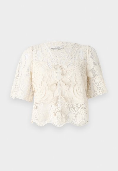 Crème kanten blouse met korte pofmouwen, een scalloped zoom en decoratieve strikdetails aan de voorkant. Fijn bloemmotief over de gehele blouse.