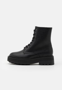 Botas de tobillo de cuero negro con punta redondeada, diseño de cordones, ojales metálicos y suela gruesa y texturizada. Material suave, adornos mínimos.