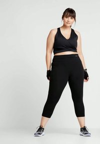 Fekete sportmelltartó, V-nyakú és rövidített fazonú, fekete 3/4-es leggingszel párosítva. Az öltözet sima, testhezálló vonalvezetéssel rendelkezik.