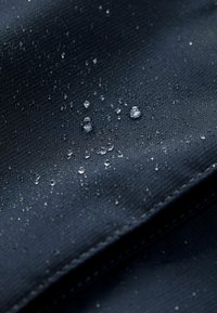 Water-repellent navy fabric featuring small water droplets on a textured surface, with visible stitching along the edges.