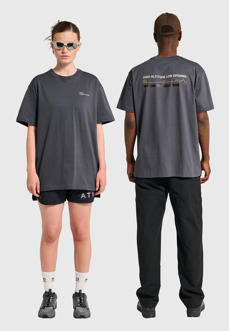 Szary t-shirt z krótkim rękawem z logo z przodu i napisem z tyłu. Połączony z czarnymi szortami, teksturowaną tkaniną i kontrastującym obuwiem.