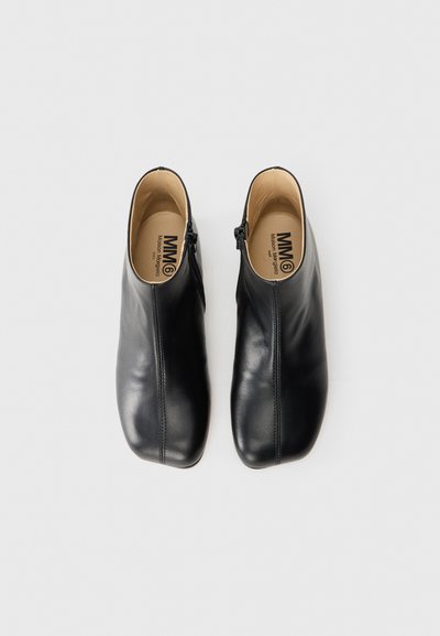Svarta läderankelboots med en slät yta, dragkedjestängning på ena sidan och en rund tådesign. Inuti har de en ljusbeige foder.