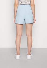 Světle modré šortky s hladkým povrchem, mají zadní kapsy a čistou siluetu. V kombinaci s bílými teniskami.