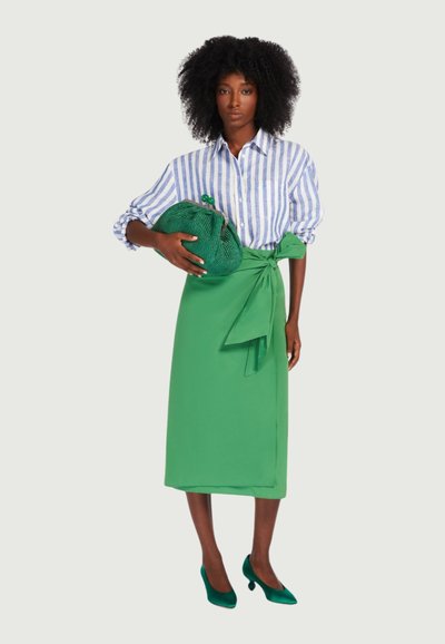 Gestreiftes blau-weißes Hemd, grüner Wickelrock mit Schleifendetail, dazu passende grüne geflochtene Clutch und grüne Absatzschuhe. Glatte Oberfläche insgesamt.
