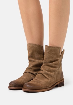 Bottines en cuir marron avec un design décontracté, texture perforée, bout arrondi et talon en bois. Les bords présentent des détails de couture à cru.