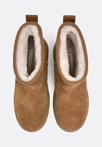 Brązowe zamszowe botki za kostkę z miękką białą futrzaną podszewką, przeszyciami i pętelkami z tyłu ułatwiającymi zakładanie.