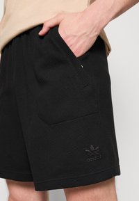 Black textured shorts featuring side pockets and an embroidered Adidas logo on the lower left. Material is lightweight and woven.