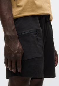 Μαύροι σορτς από ελαφρύ υλικό, με φερμουάρ σε πλαϊνή τσέπη, ελαστική μέση και ρυθμιζόμενο κορδόνι.