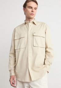 Beige langarm overhemd met knopen, gemaakt van katoen, met twee borstzakken en een zachte, gladde structuur. Slim fit met een minimalistisch ontwerp.