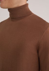 Rjav pulover s Turtleneck iz gladkega pletenega materiala. Ima prilegajoč dizajn z visokim ovratnikom in rebrastimi detajli na vratu.