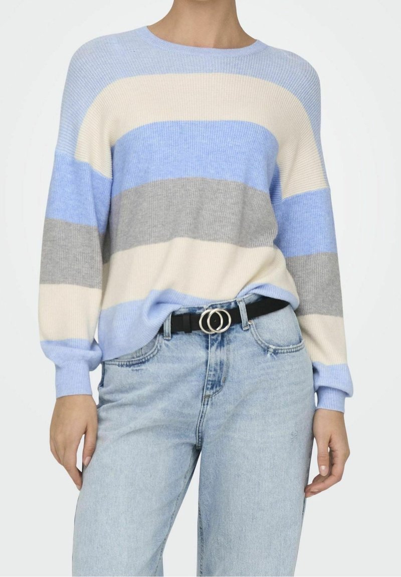 Personne portant un pull rayé bleu pastel, gris et crème rentré dans un jean bleu clair avec une ceinture noire ornée de deux anneaux argentés.