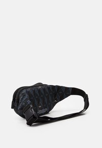 Black fabric sling bag with a geometric blue pattern, dual zippered compartments, and an adjustable strap. Includes a logo detail.