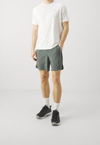 Camiseta deportiva blanca de manga corta, pantalones cortos grises con paneles laterales, calcetines blancos y zapatillas negras. Los tejidos parecen ligeros y transpirables.