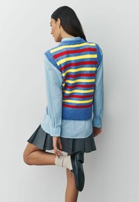 Farebný pletený sveter s modrými, červenými, žltými a bielymi pruhmi, nosený cez svetlomodrú košeľu a šedú plisovanú sukňu. Má rebrované okraje.