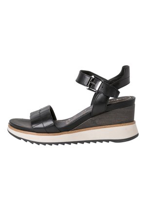 Sandale à talon noire avec bride de cheville ajustable, tige en cuir cousue, détail en liège et semelle rayée blanche et noire.