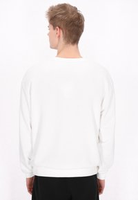 Vit sweatshirt med en avslappnad passform, rund halsringning och ribbad mudd, med slät tyg och en enhetlig färg utan mönster.