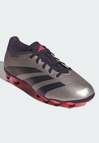 Botín de fútbol gris con detalles negros y suela rosa. Presenta una textura perforada y diseño con cordones. Marca "Predator" en el lateral.