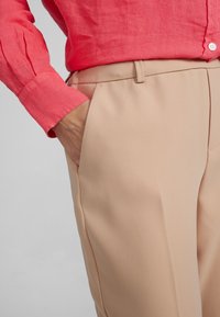 En närbild av ett persikofärgat par byxor med sidoficka, kombinerat med en ljus korallfärgad långärmad skjorta med manschettdetaljer.