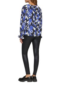 Bloes met bloemenpatroon in blauw, wit en zwart. Gecombineerd met glanzende zwarte leggings en chunky zwarte loafers. Relaxte pasvorm.