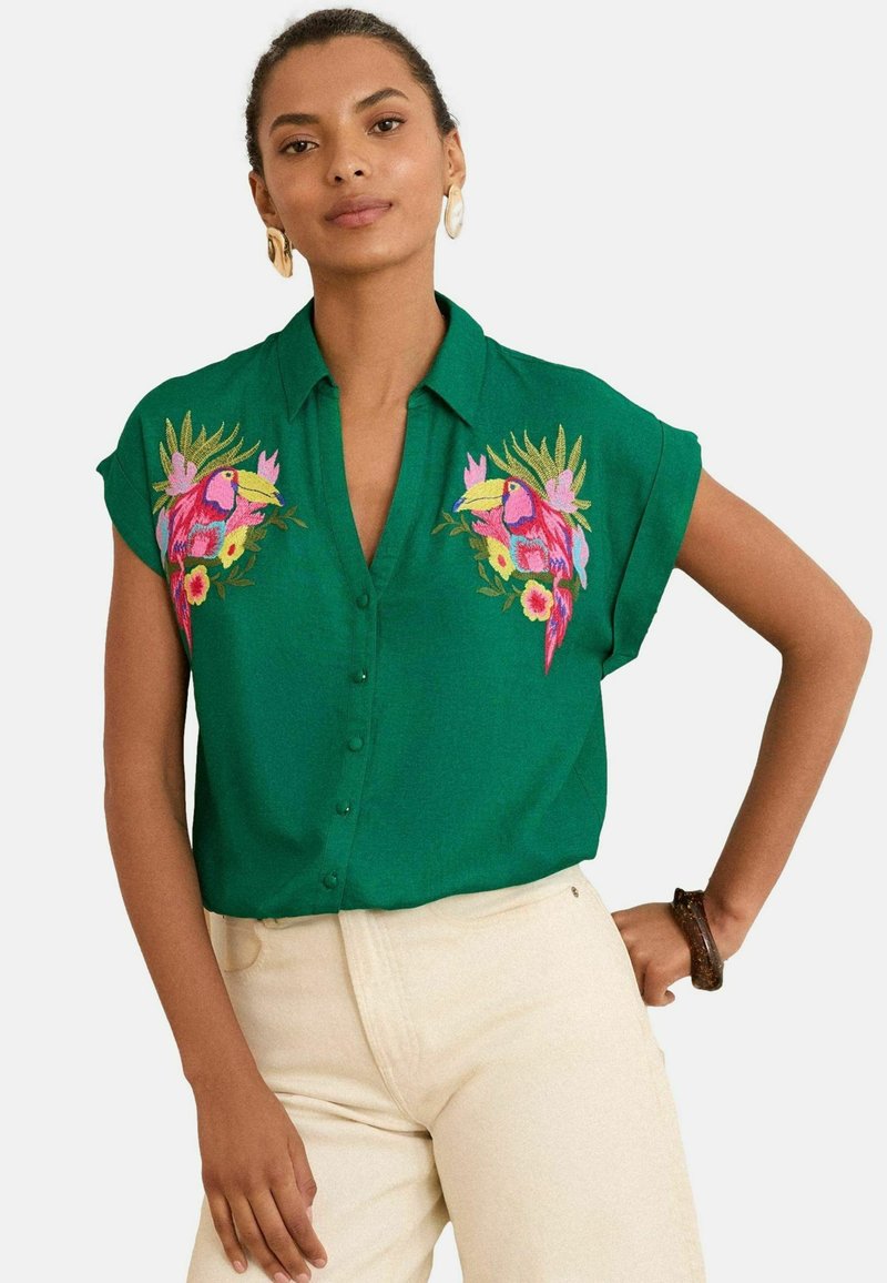 Blusa verde con cuello y mangas cortas, que presenta vibrantes tucanes bordados y diseños florales en el pecho. Cierre frontal con botones.