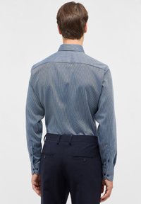 Marineblauwe gedessineerde blouse met lange mouwen, knoopmanchetten en een standaardkraag. Het materiaal lijkt glad met een subtiele glans.