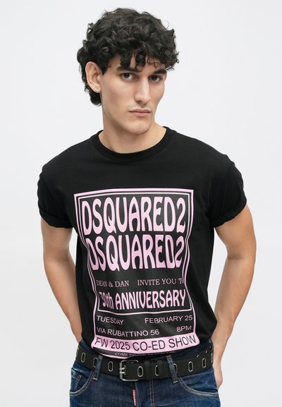 Camiseta de algodón negra con texto gráfico en rosa neón. Presenta mangas enrolladas y una textura suave. El texto incluye detalles del evento y el nombre de la marca.