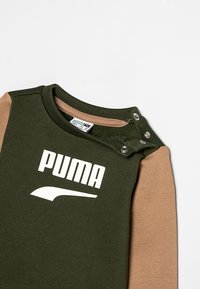 Camisa de manga larga verde y marrón con un logo blanco de "PUMA", cierres a presión en el hombro y una textura suave de algodón.