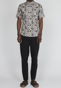 Koszula z krótkim rękawem z guziczkami w jasnym beżu z kwiatowym nadrukiem w granatowym i białym kolorze. Połączona z czarnymi spodniami i brązowymi sandałami.