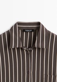 Gestreepte shirt in donkerbruin met crèmekleurige verticale lijnen. Heeft een kraag, knoopsluiting aan de voorkant en een borstzak. Zacht, lichtgewicht stof.