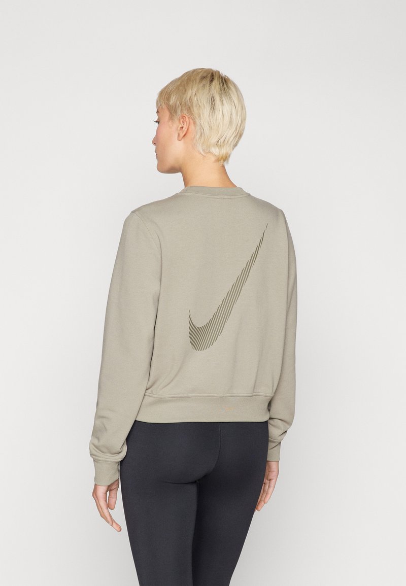 Felpa kaki con texture a coste, caratterizzata da un grande logo Nike swoosh tono su tono sulla schiena e collo rotondo. Abbinata a leggings neri.