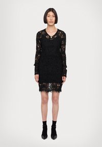 Abito in pizzo nero con scollo a V, maniche lunghe, intricate fantasie floreali e un orlo smerlato con dettagli di perline.