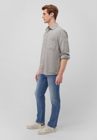 Gray button-up shirt with a single chest pocket, paired with medium blue jeans and white sneakers with green accents, shown side view.