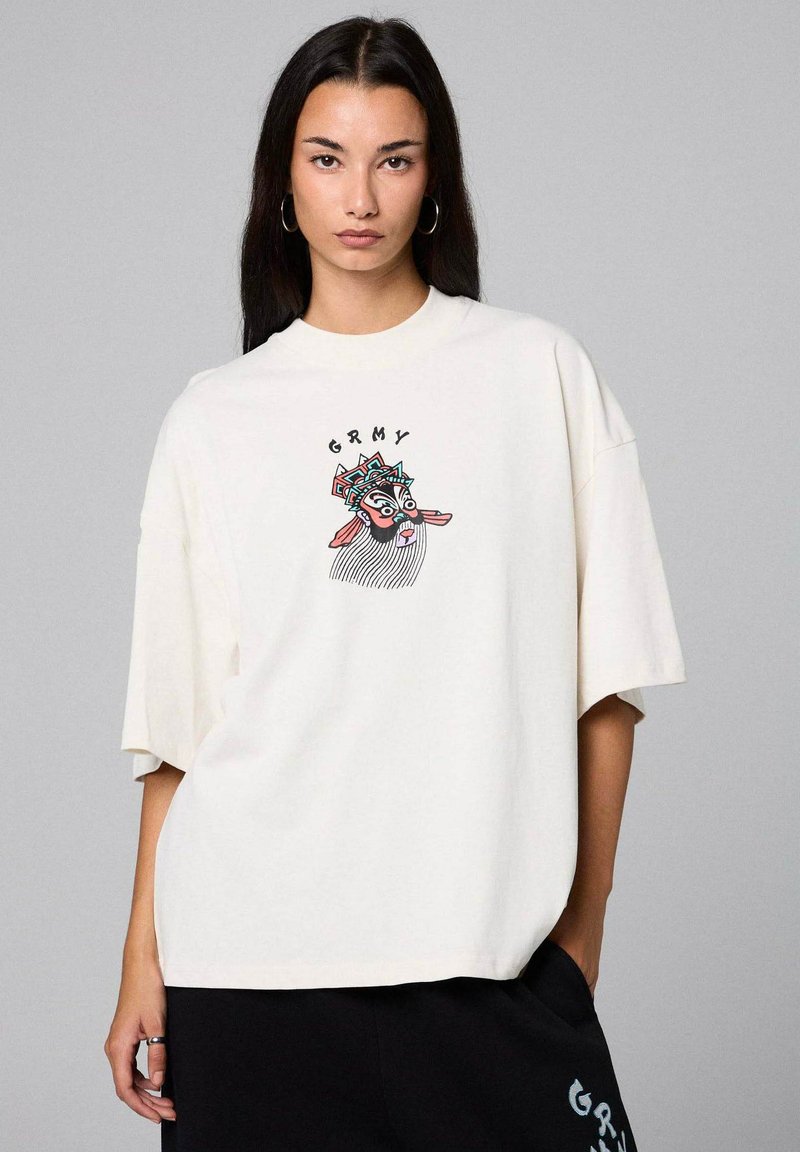 Camiseta de gran tamaño en color crema de algodón con un gráfico colorido de un rostro y el texto "GRMY" en el pecho. Manga corta y corte relajado.