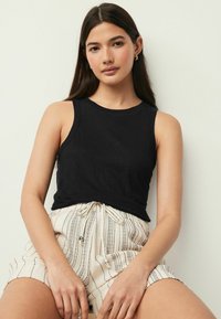 Top sans manches noir en tissu doux, avec un décolleté rond. Porté avec un short crème rayé à taille nouée et texture à motifs.