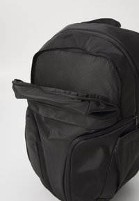 Zaino nero realizzato in materiale sintetico liscio. Presenta una tasca esterna con zip e un design strutturato e arrotondato. Cuciture durevoli in vista.