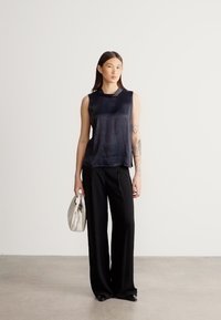 Čierny tielkový top s hladkou, lesklou textúrou, skombinovaný s čiernymi nohavicami s vysokým pásom a svetlosivou kabelkou.